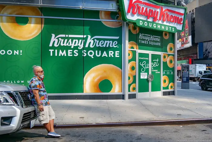 A photo of a man leaning on a car in front of a Krispy Kreme in Times Square